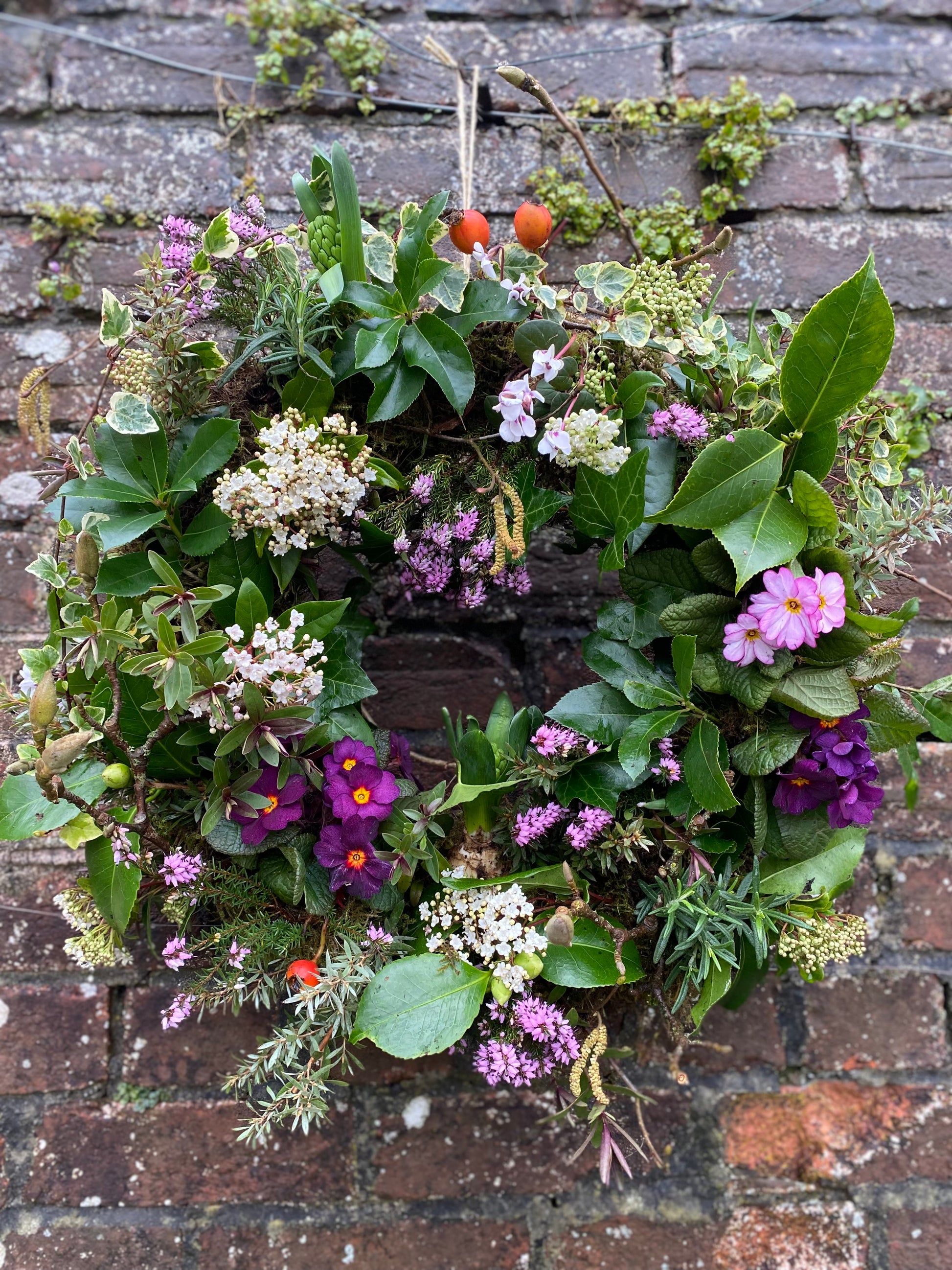Floral wreath with greenery and colorful flowers on a brick wall
